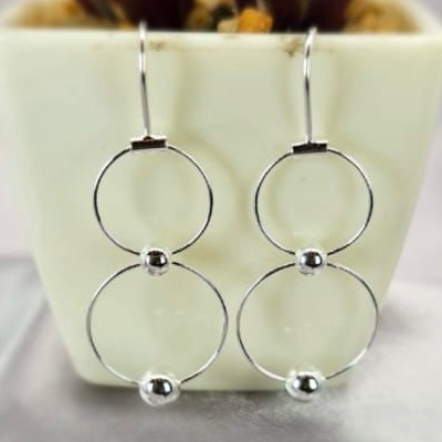A pair of sterling silver hoop drop earrings displayed on a surface with a white and green plant in the background.