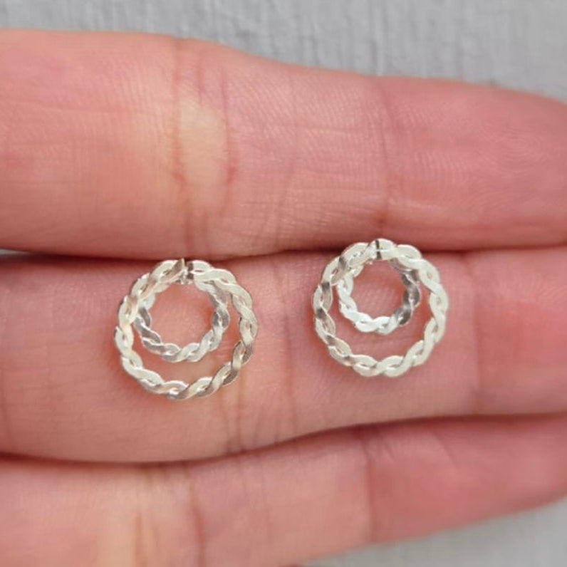 Two silver hoop earrings held between fingers on a neutral background