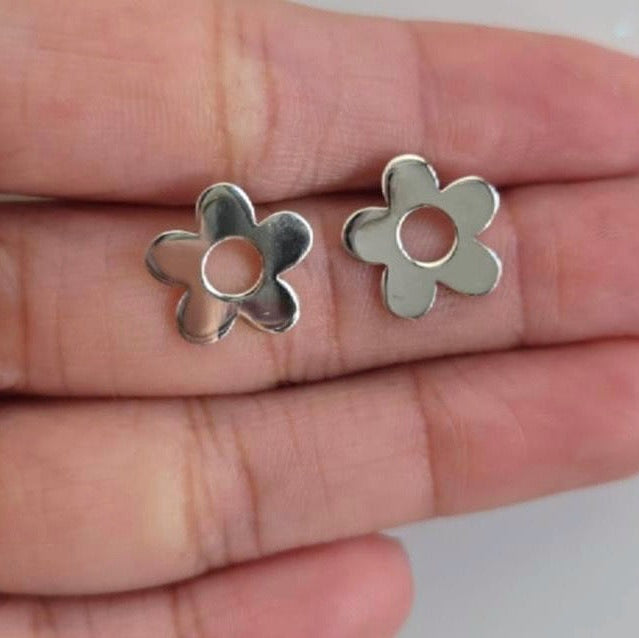 Silver flower-shaped earrings held between fingers on a light background