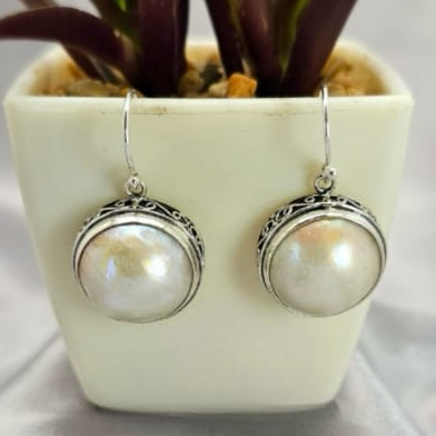 A pair of white Mabe pearl drop earrings in a sterling silver setting, displayed in a white vase with a green plant.
