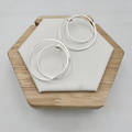 A pair of large sterling silver double hoop earrings displayed on a wooden stand with a white cushion.