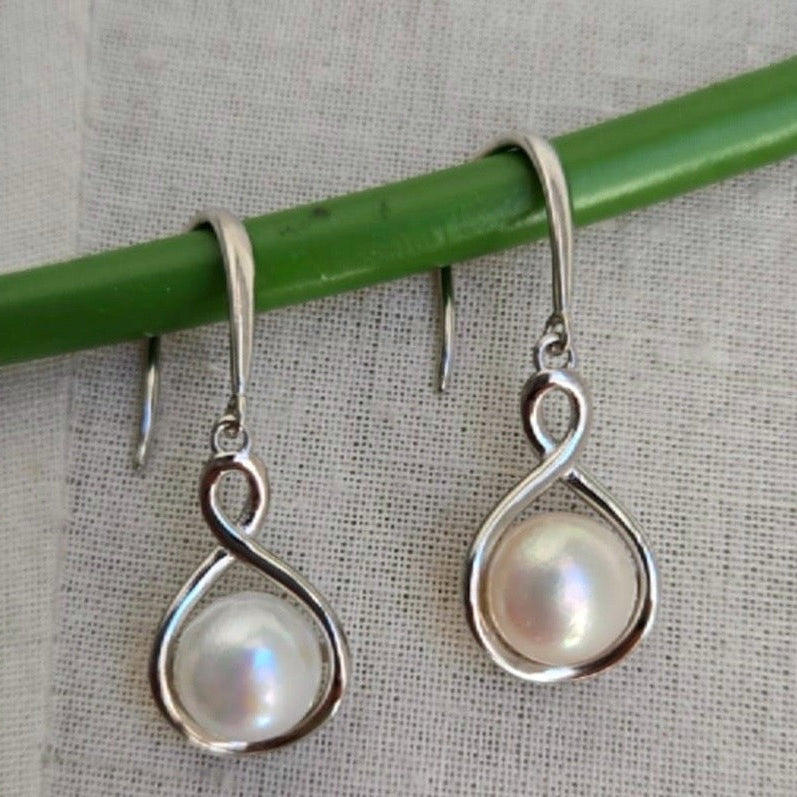 Silver earrings with pearl-like stones hanging on a green stick against a textured gray background