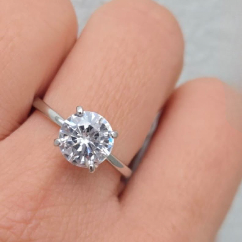 Silver ring with a large diamond on a finger against a neutral background