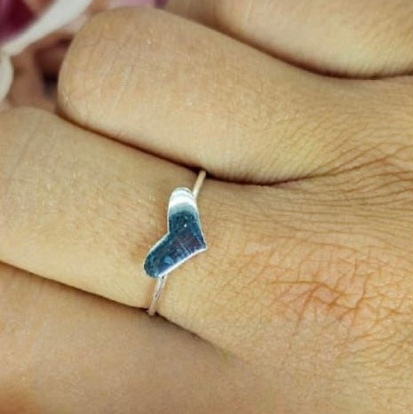 A person's hand displaying a sterling silver flat heart ring on their finger.