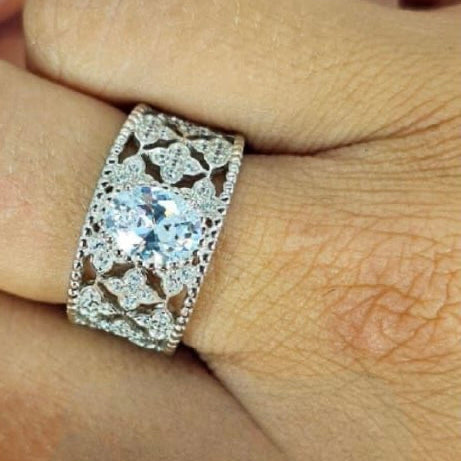 A woman's hand displaying a silver lace filigree ring with a central cubic zirconia gem surrounded by smaller clear cubic zirconia pieces set in a white gold-colored band.