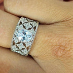 A woman's hand displaying a silver lace filigree ring with a central cubic zirconia gem surrounded by smaller clear cubic zirconia pieces set in a white gold-colored band.