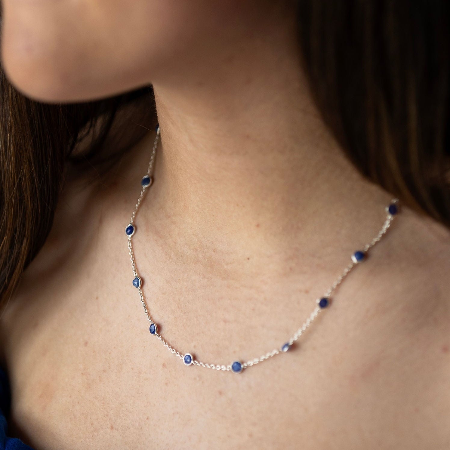 A close-up image of a sterling silver necklace with blue semi precious stones embedded in it, worn by a person.