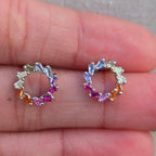 Pair of small hoop earrings with multicolored gemstones on a hand.