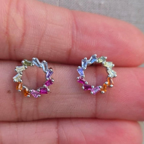 Pair of small hoop earrings with multicolored gemstones on a hand.