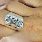 A person's hand displaying a silver ring with five cubic zirconia stones set in a wave design.