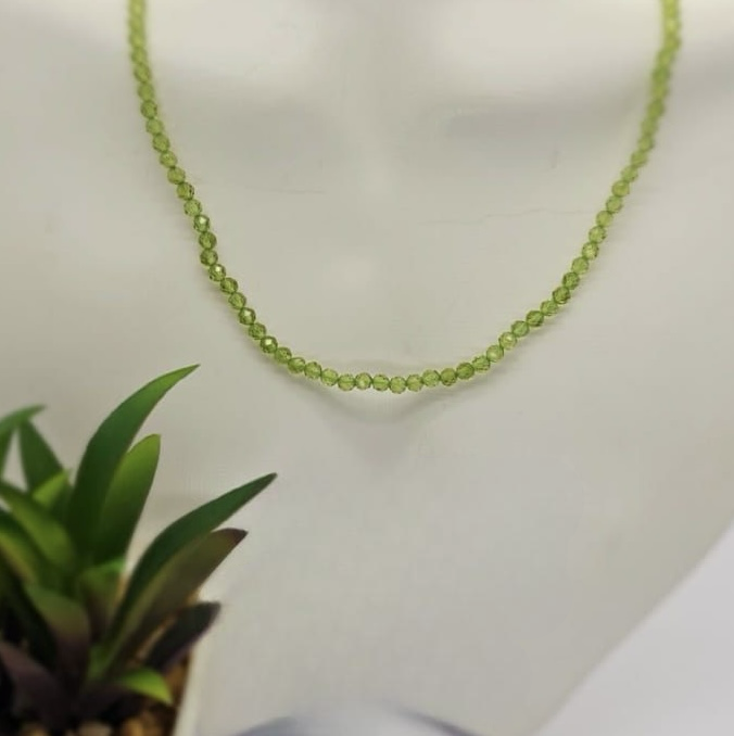 A peridot semi precious stone necklace with a sterling silver clasp displayed on a mannequin.