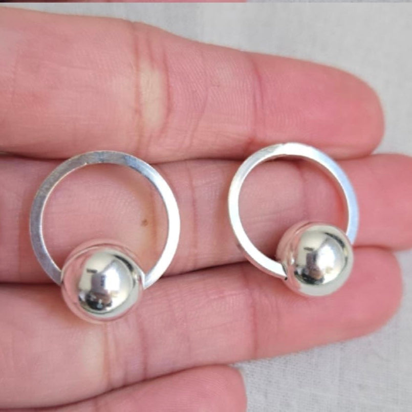 Silver hoop earrings with spherical ends held between fingers on a light background