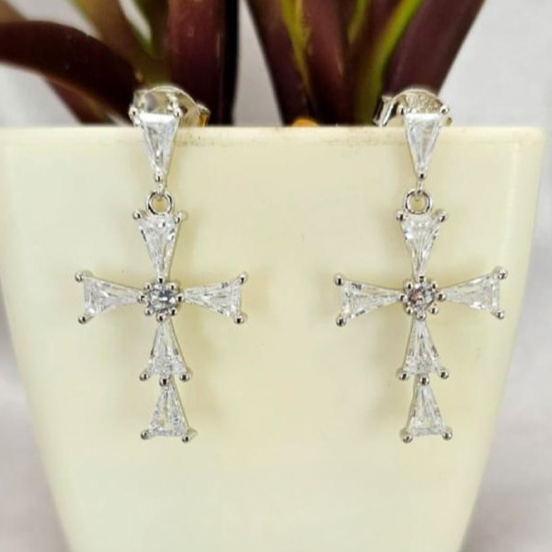 Silver cross earrings with clear stones on a light surface with a plant in the background