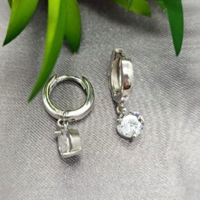 Silver hoop earrings with clear gemstones on a gray surface with green leaves in the background