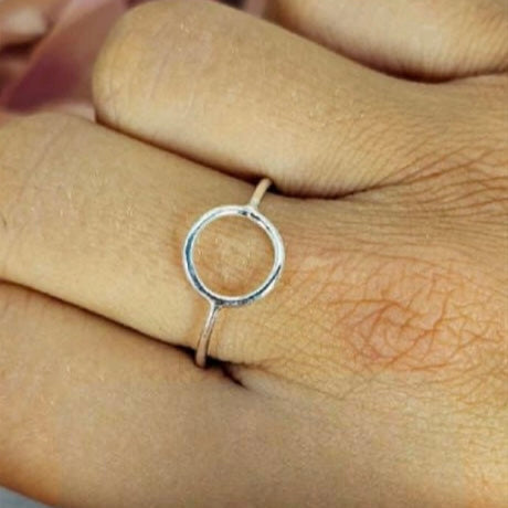 A sterling silver ring with a simple circle detail on top, displayed on a person's finger.
