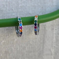 Hoop earrings with colorful gemstones on a green stick against a gray background
