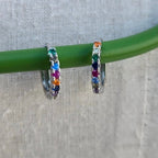 Hoop earrings with colorful gemstones on a green stick against a gray background