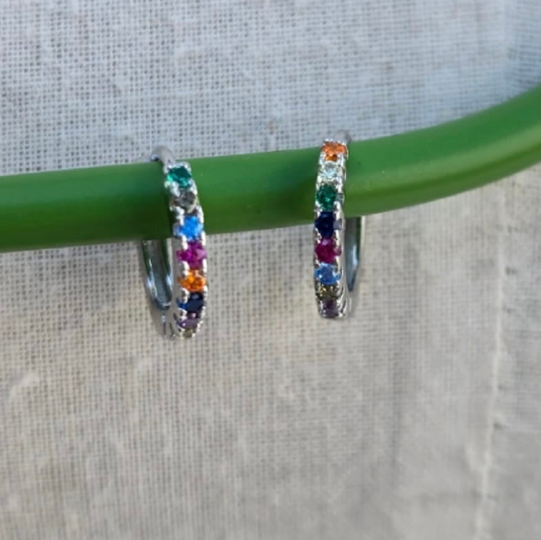 Hoop earrings with colorful gemstones on a green stick against a gray background