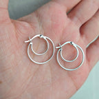 Silver hoop earrings held in a hand against a neutral background