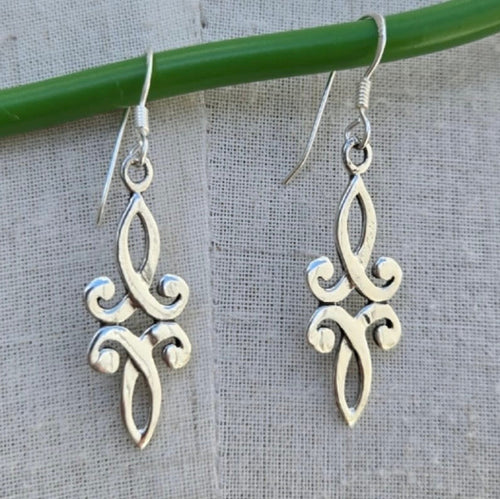 Silver filigree earrings hanging from a green stick on a textured gray background