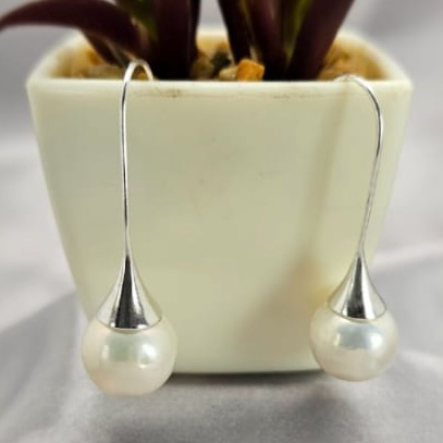 A pair of sterling silver drop earrings with freshwater pearl embellishments, displayed in a white vase with green foliage in the background.
