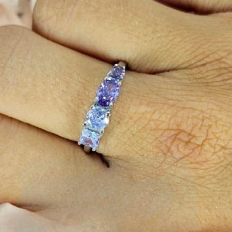A sterling silver ring with purple cubic zirconia stones, held on a person's finger.