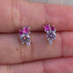 Pair of pink gemstone earrings held between fingers on a light background