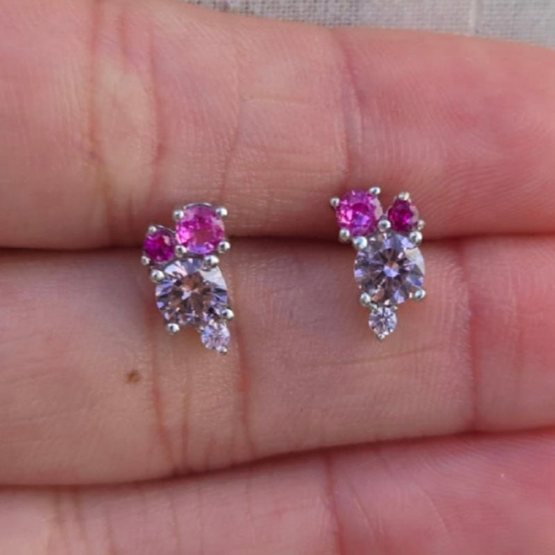 Pair of pink gemstone earrings held between fingers on a light background