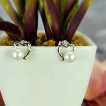 Heart-shaped stud earrings with freshwater pearls, displayed in a white pot with green leaves.