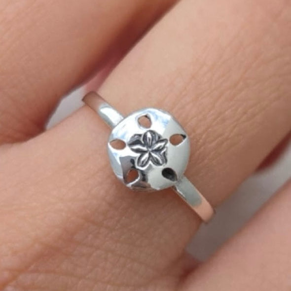 Silver ring with a floral design on a finger against a neutral background