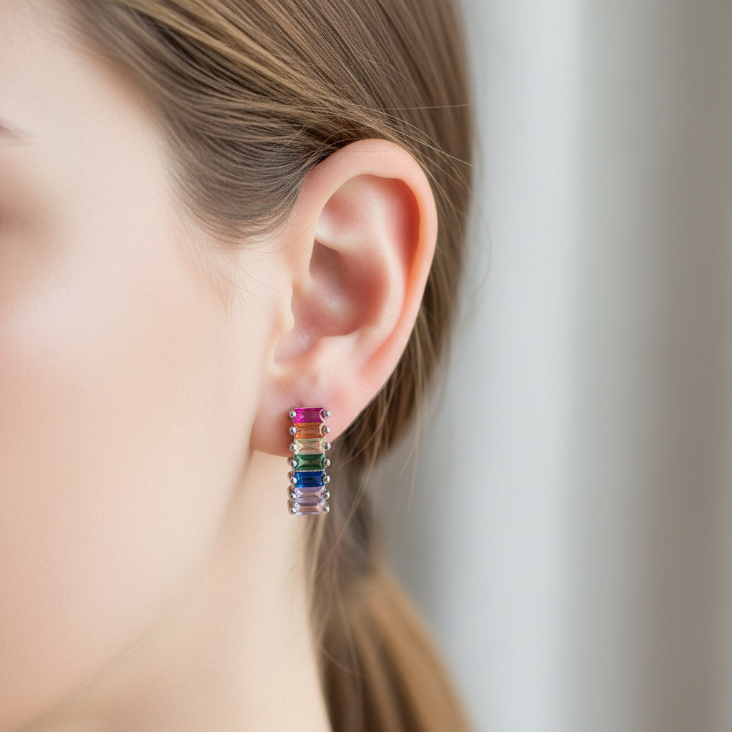 Rainbow-colored earrings held between fingers against a neutral background