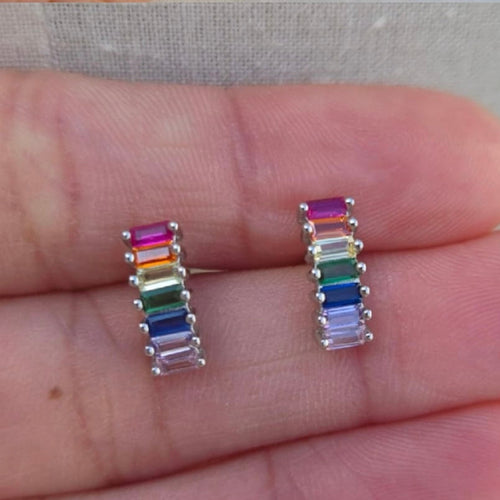 Rainbow-colored earrings held between fingers against a neutral background