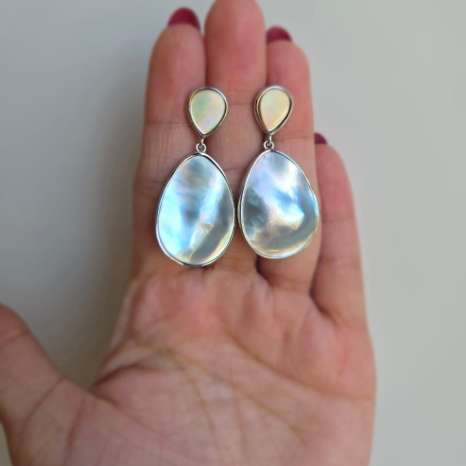 A pair of double oval drop blister mabe pearl earrings held in a person's hand, with a silver setting.