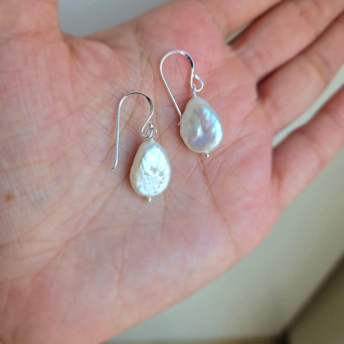 A pair of teardrop freshwater pearl hook earrings placed on a person's hand, showcasing the luster and shape of the pearls.