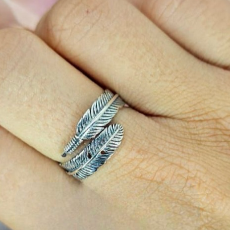 An adjustable sterling silver feather ring worn on a person's finger, showing the ring's detail and fit.