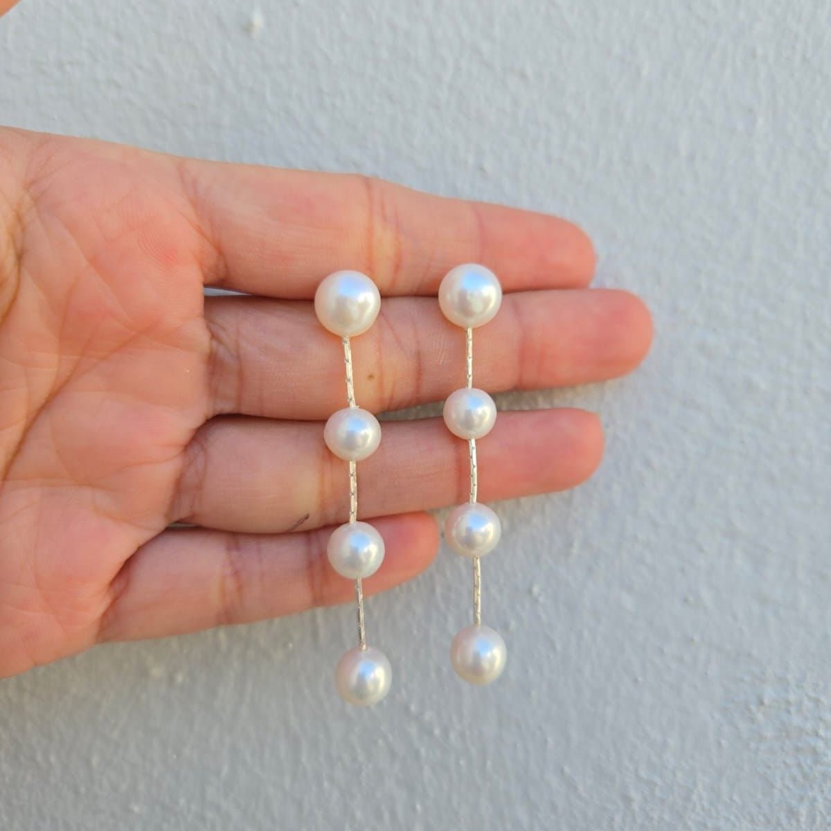 Pearl earrings held between fingers against a light background