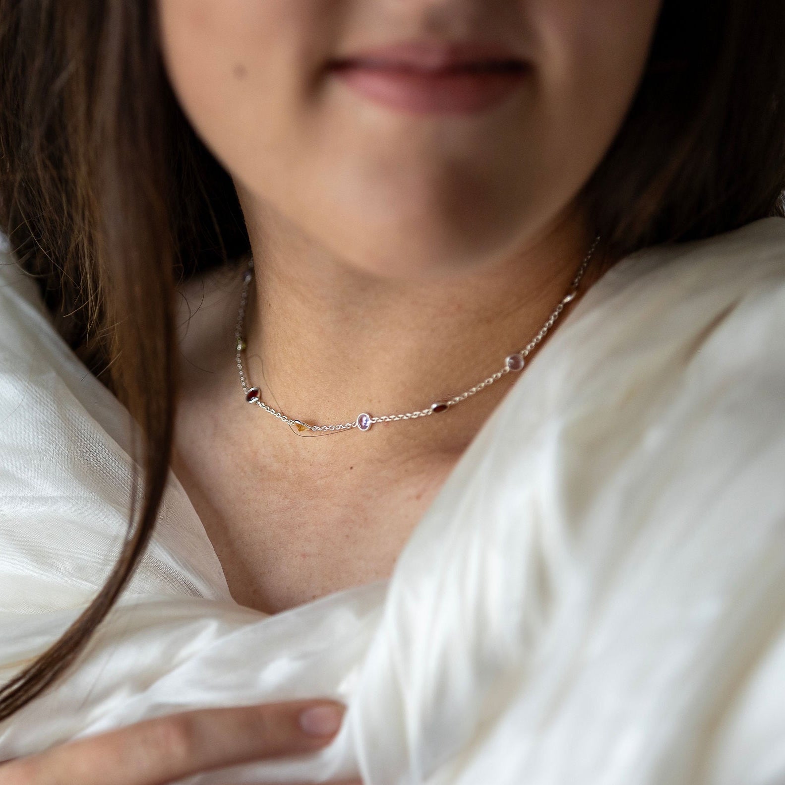 A person wearing a sterling silver necklace with embedded semi precious stones in a white fabric.