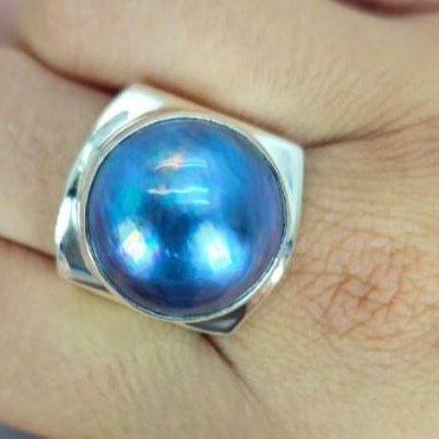 A blue Mabe pearl ring set in sterling silver, displayed on a person's finger.