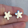 Star-shaped silver earrings held between fingers against a neutral background