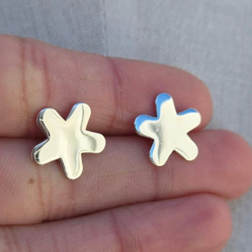 Star-shaped silver earrings held between fingers against a neutral background