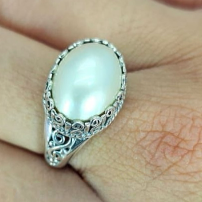 An oval freshwater pearl ring with filigree setting on a hand.