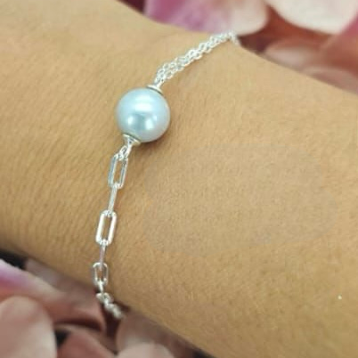 A sterling silver bracelet with a grey freshwater pearl on a person's wrist, with a floral background.
