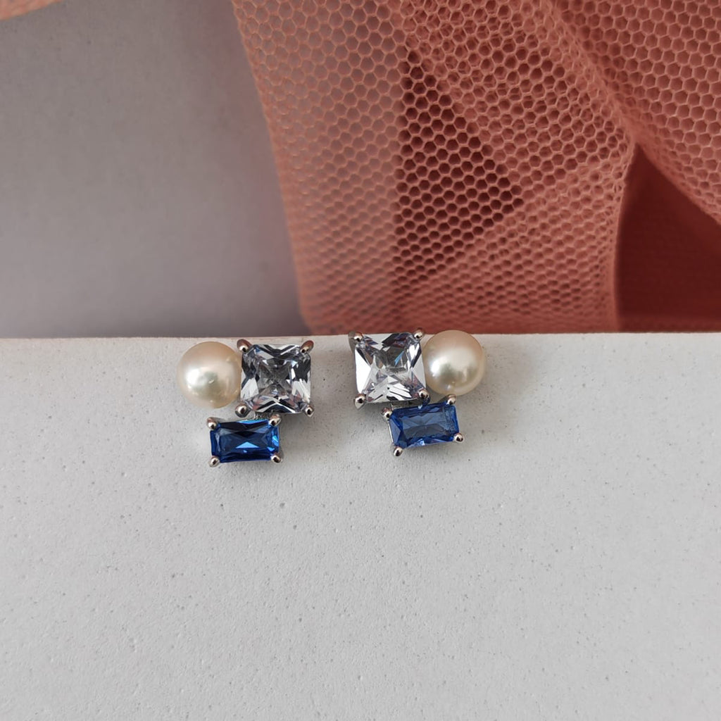 Pair of earrings with pearls and blue gemstones on a light gray surface.