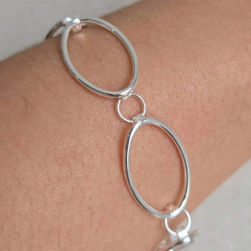 Silver bracelet with interlocking rings on a wrist against a neutral background