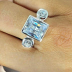 A sterling silver ring with a large square cubic zirconia and two round ones, displayed on a person's finger.