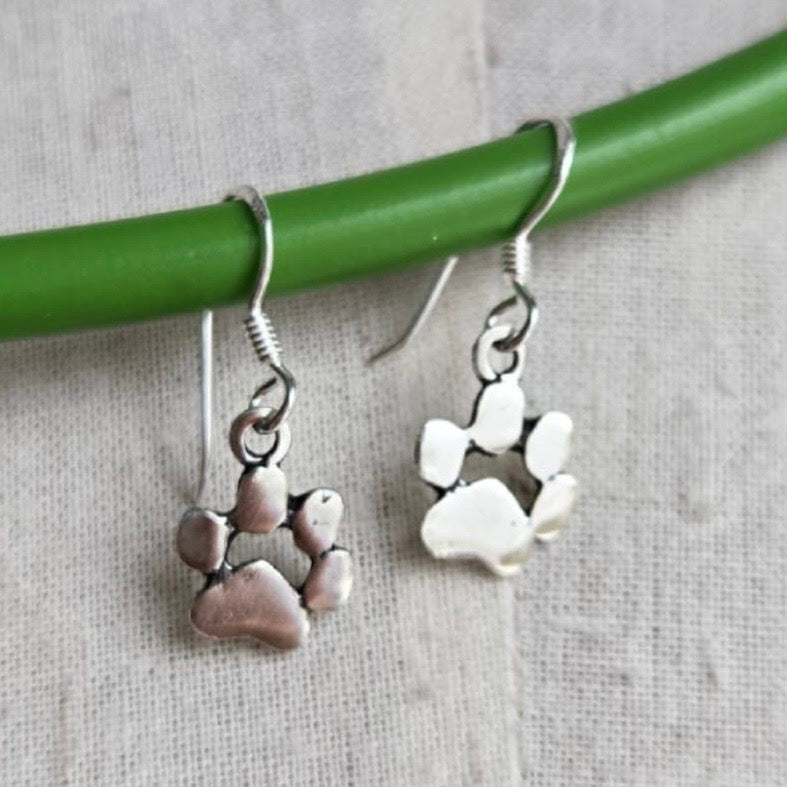 Silver paw print earrings on a green stick against a gray background