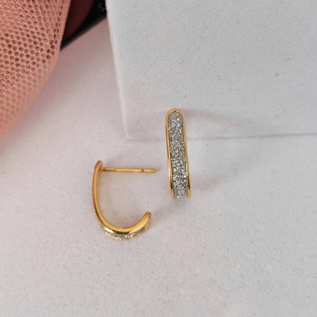 Gold hoop earrings with embedded stones on a light pink surface