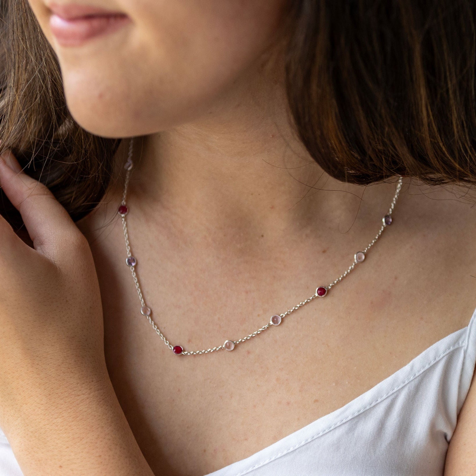 A person wearing a sterling silver necklace with red and semi-precious stones.