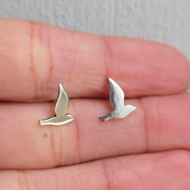 Silver bird-shaped earrings on a person's hand