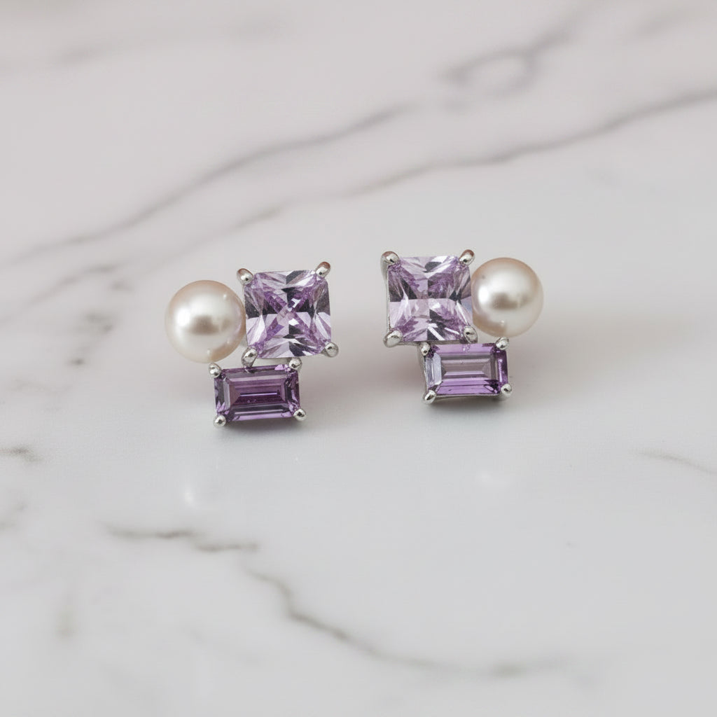 Pair of earrings with purple and pearl stones on a light surface.